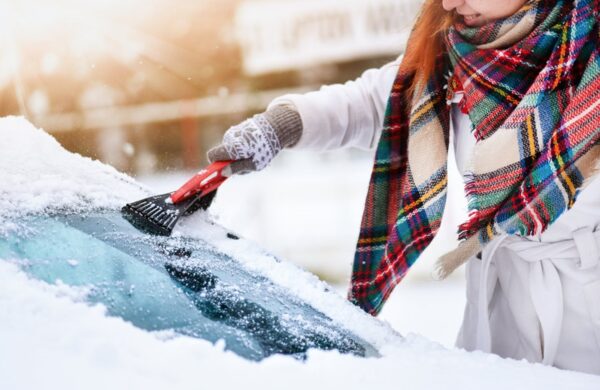 Eine Frau, die Frost von einer Autoscheibe kratzt